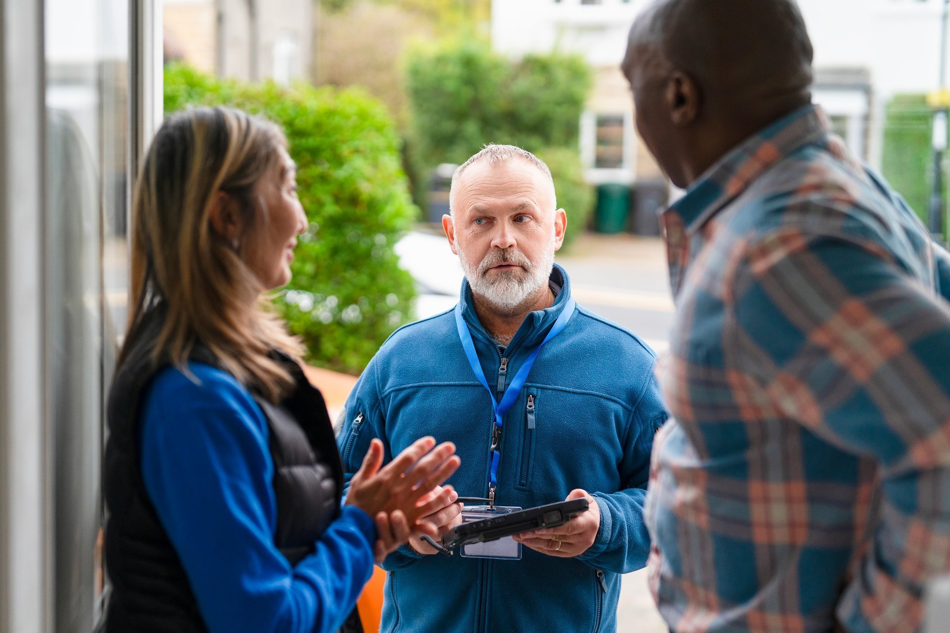 Two community members discuss with a service provider outside a building on a sunny day, sharing ideas and solutions for local needs in their neighborhood